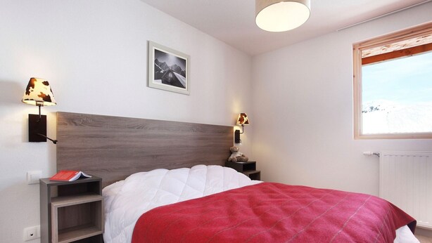 A bedroom with a bed, a nightstand, a lamp, a teddy bear, a framed picture, and a window with a view. - Chalet in Paradiski with Pool & Spa (Plagne Villages)