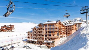 A multi-story wooden building with balconies, ski lift cables, and a snowy mountain backdrop. - Chalet in Paradiski with Pool & Spa (Plagne Villages)