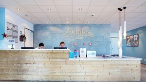 A reception desk with a wooden finish, a wall-mounted sign reading 'Odalys,' and a bulletin board with various notices. - Chalet in Paradiski with Pool & Spa (Plagne Villages)