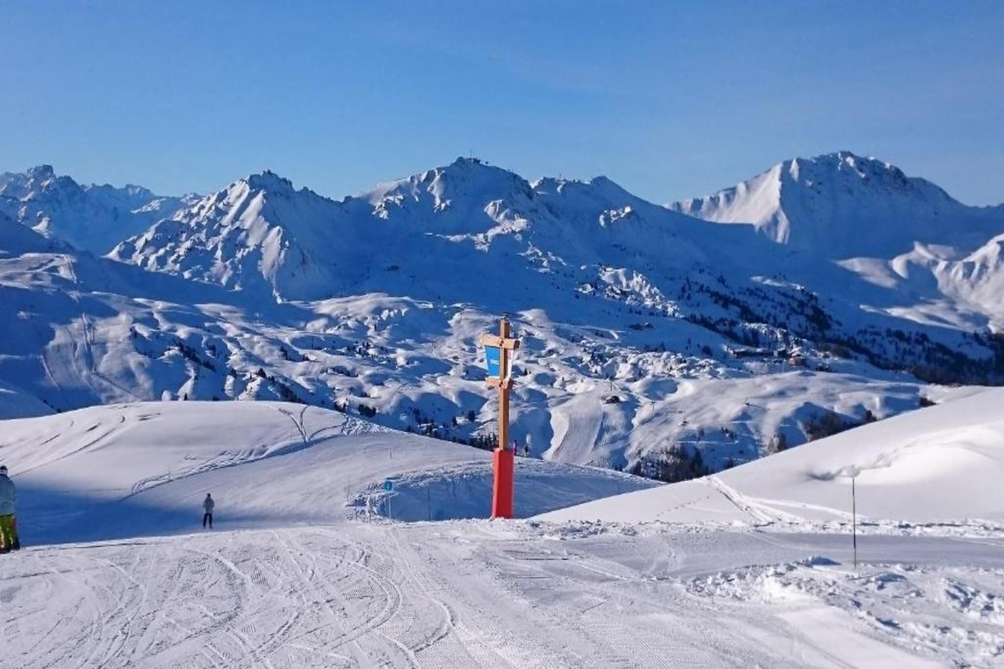 A snowy mountain landscape with a ski lift tower and tracks.