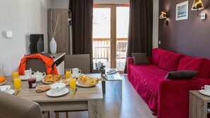 A modern living room with a red sofa, a dining area with breakfast items, and a balcony with a view. - Chalet in Paradiski with Pool & Spa (Plagne Villages)