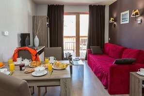 Ein modernes Wohnzimmer mit einem roten Sofa, einem Essbereich mit Frühstücksangebot und einem Balkon mit Blick.