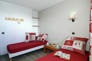 A room with two single beds, a small table with a book and a cup, and a wall-mounted light fixture. - Apartment by Table Verte Lift (Les allues)