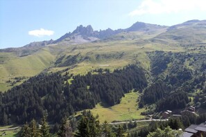 A mountainous landscape with a forested valley, a small building, and a distant peak.
