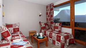 A cozy room with a sofa and a bed, both covered in red and white patterned blankets. There's a small wooden table with a kettle and glasses, and a window with curtains. - Apartment by Table Verte Lift (Les allues)