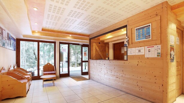 A reception area with wooden walls, a reception desk, a bench, and a view of trees through large windows.
