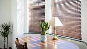 A round wooden table with a potted plant and a lamp, positioned near a window with blinds. - Arthouse Lovely Spacious 5 bed house (Nottingham)