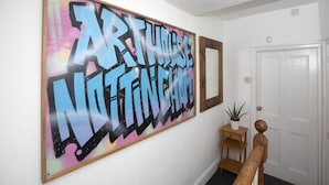 A hallway with a large graffiti-style artwork on the wall, a wooden bench, a potted plant, and a white door. - Arthouse Lovely Spacious 5 bed house (Nottingham)