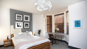 A bedroom with a bed, bedside tables, a desk, and a chair. There are four framed pictures on the wall. - Arthouse Lovely Spacious 5 bed house (Nottingham)