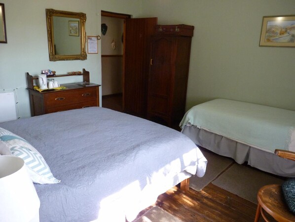 A bedroom with a large bed, a smaller bed, a wooden wardrobe, a desk with a mirror, and a painting on the wall.