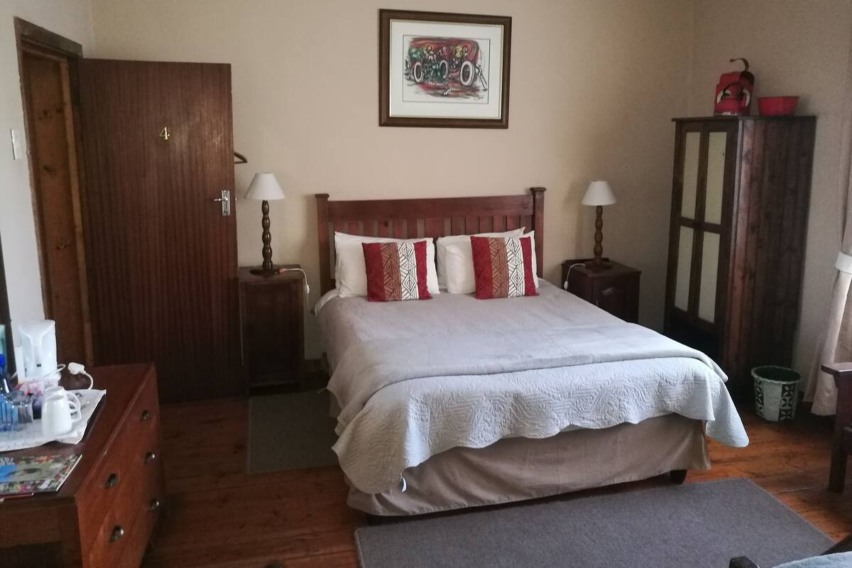 Quarto com cama, mesas de cabeceira, cômoda, porta e um quadro na parede.