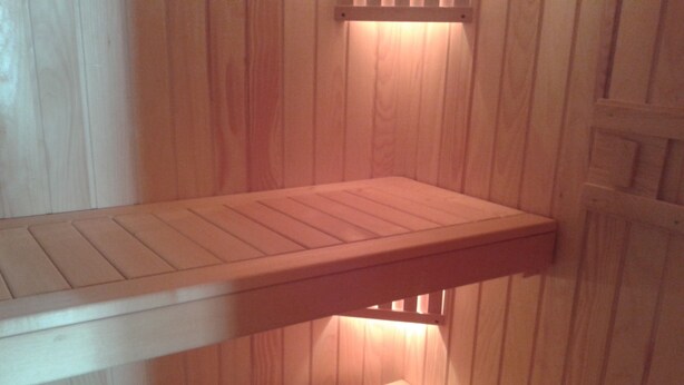 Een houten bank met een lattenstructuur, bevestigd aan een wand met verticale houten panelen.