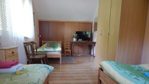 Een slaapkamer met twee bedden, een bureau, een televisie en een kledingkast.
