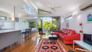 A modern kitchen with a bar area, a red leather sofa, and a dining set. - Moffat Retreat Stylish 3BR Beach Home (MOFFAT BEACH)