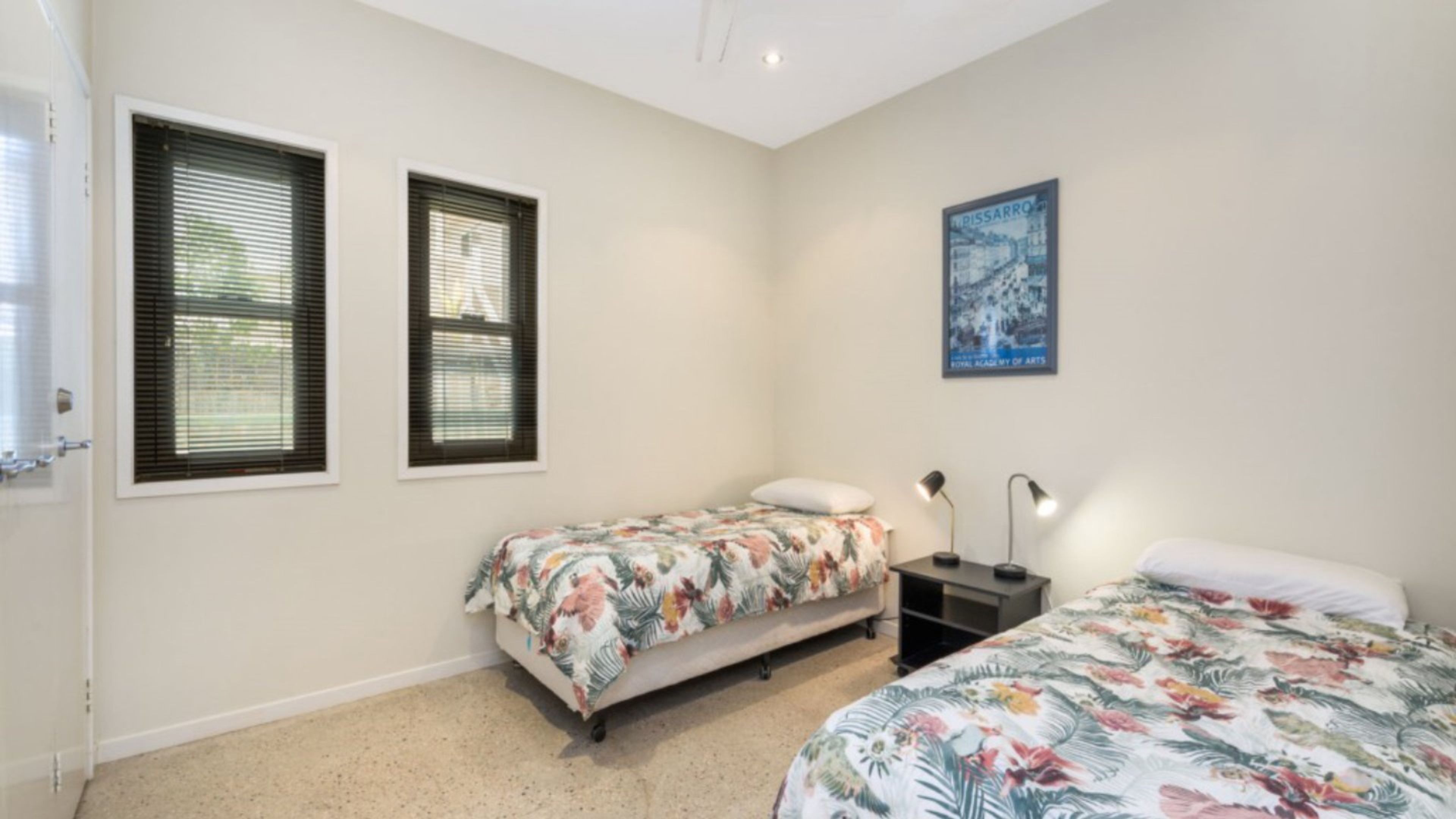 A bedroom with two beds, a nightstand, a lamp, and a wall-mounted picture.