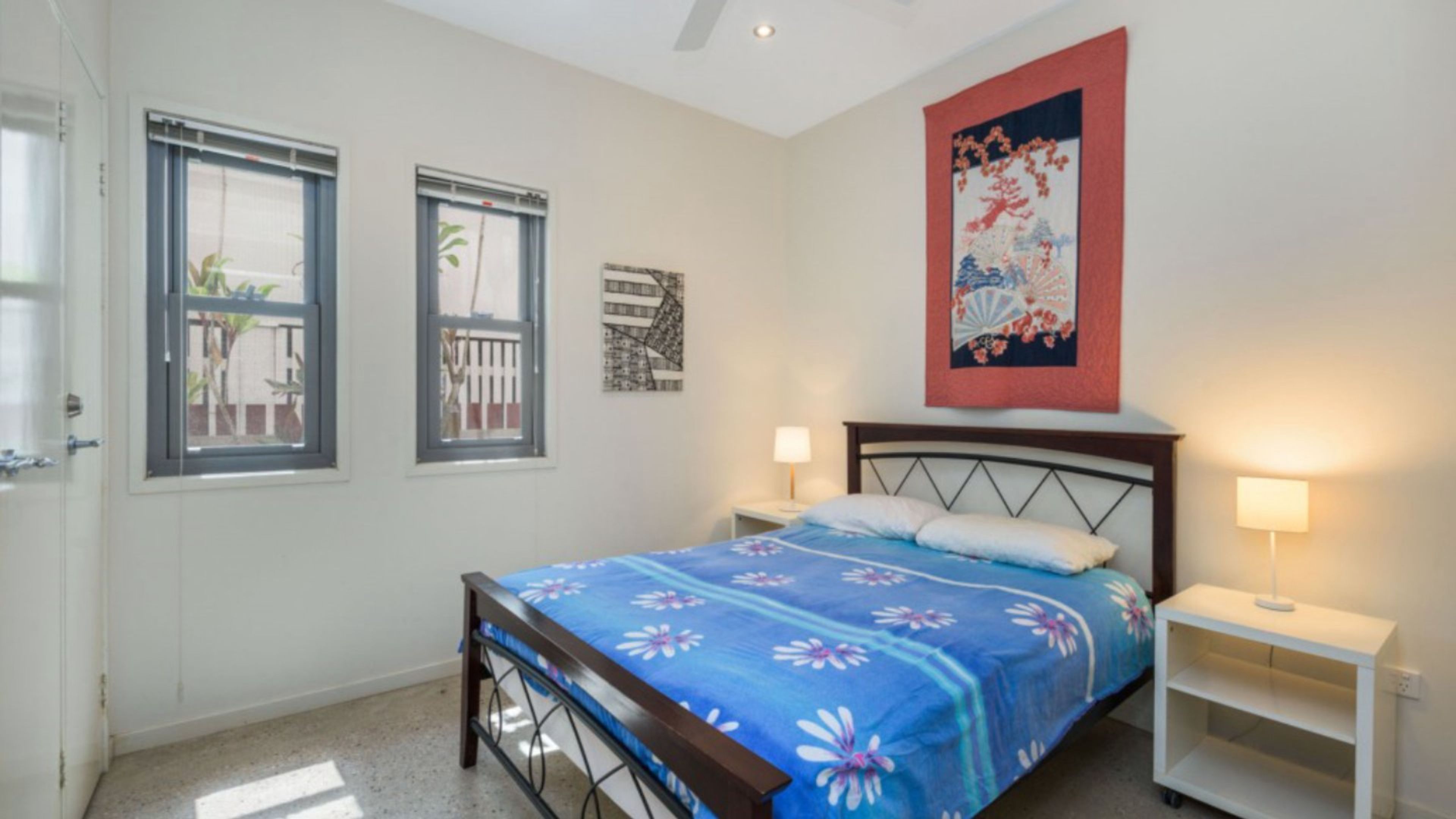 A bedroom with a bed, two bedside lamps, a nightstand, a window with a view, and a wall-mounted artwork.