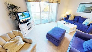 A living room with a television, a sofa, a coffee table, and a balcony with outdoor furniture.