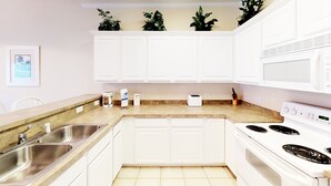 A kitchen with white cabinets, a double sink, a stove, and a microwave.