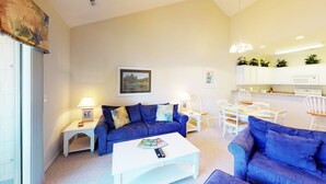 A living room with a blue sofa, a white coffee table, and a dining area with white chairs.