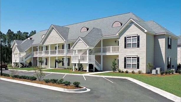 A multi-story hotel with a central courtyard, balconies, and a parking area. - Golf Villa in Little River (K102) (Little River)