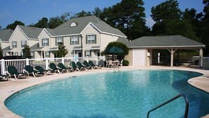 A swimming pool with lounge chairs and a covered area, surrounded by a white fence and a building with multiple windows. - Golf Villa in Little River (K102) (Little River)