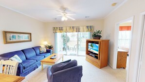 A living room with a blue sofa, a wooden TV stand, and a ceiling fan. - Golf Villa in Little River (K102) (Little River)