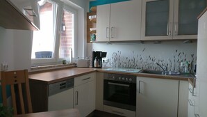 A compact kitchen with white cabinets, a built-in oven, a dishwasher, and a window with a view of a brick building.