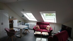 A modern loft bedroom with a sloped ceiling, skylights, a red sofa, a small table, and a TV.