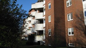 A multi-story brick building with balconies, a clear sky, and some greenery.