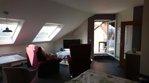A room with a sloped ceiling, skylights, a television, a dining table, and a chair.