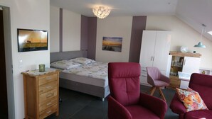A bedroom with a bed, a wooden dresser, a red armchair, a pink chair, and a cabinet.
