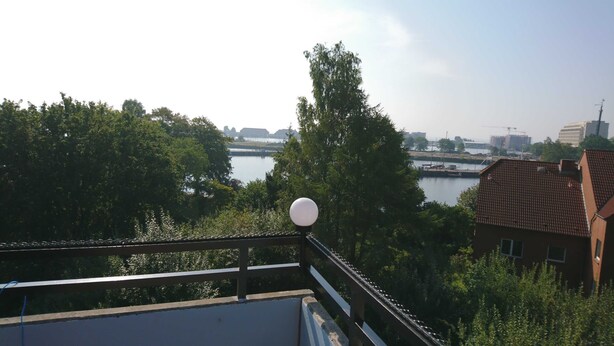 A view from a balcony overlooking a river with trees and buildings in the background.