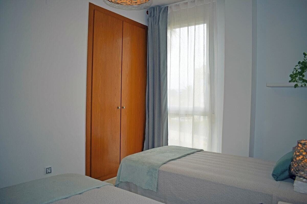 A bedroom with two beds, a wooden wardrobe, and a window with curtains.