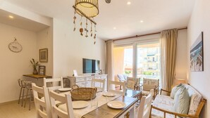 A dining area with a wooden table, white chairs, and a television on a cabinet. - Anacasa Zurich Les Marines AP3216 (Denia)