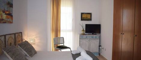 Una habitación de hotel con cama, televisión, armario y ventana con cortinas.