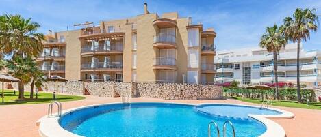 A hotel with a swimming pool, multiple balconies, and a stone wall.