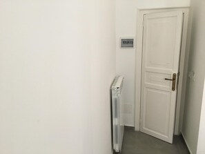 A narrow hallway with a white door, a radiator, and a light switch on the wall. - FraLePorte B&B (Palermo)