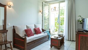 Ein gemütliches Wohnzimmer mit einer Couch, einem Holzstuhl, einem kleinen Tisch mit Büchern und einem Fernseher.