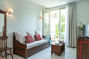 A cozy living room with a sofa, a wooden chair, a small table with books, and a television. - Peaceful Alsace Retreat (Bergheim)