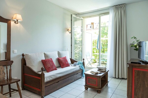 A cozy living room with a sofa, a wooden chair, a small table with books, and a television.