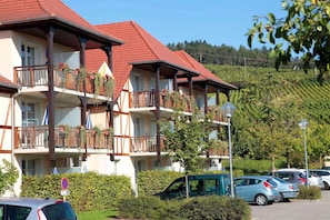 A multi-story hotel with balconies, a parking area, and a hilly landscape in the background.