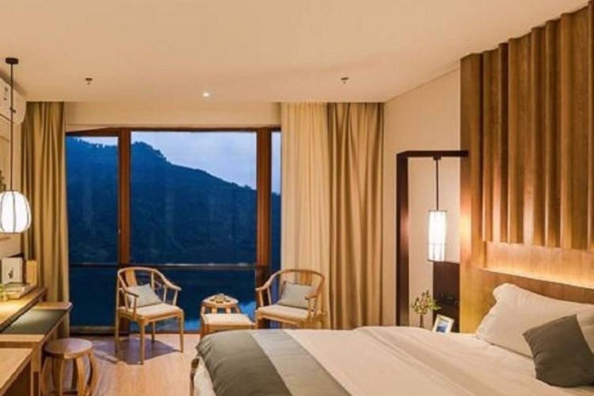 Une chambre d’hôtel avec un grand lit, deux fauteuils, un bureau et une vue sur les montagnes par une grande fenêtre.