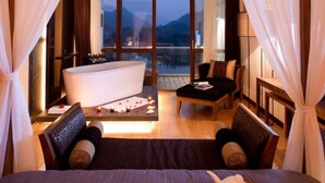 Une chambre dotée d’un grand lit, d’un coin salon avec une table et des chaises, d’une baignoire et offrant une vue sur les montagnes grâce à de grandes fenêtres.