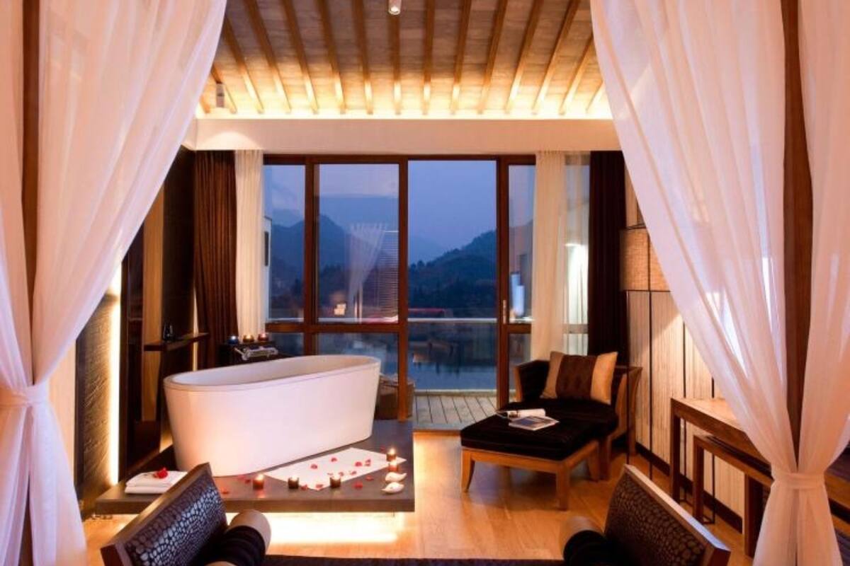 Une chambre dotée d’un grand lit, d’un coin salon avec une table et des chaises, d’une baignoire et offrant une vue sur les montagnes grâce à de grandes fenêtres.