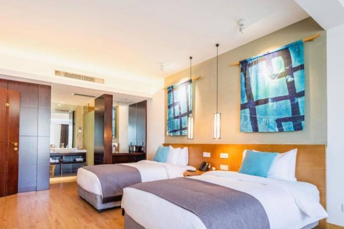 Une chambre d’hôtel avec deux lits, un plancher en bois et un grand tableau abstrait accroché au mur.
