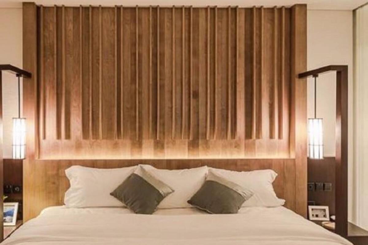 Une chambre d’hôtel avec une tête de lit en bois, un grand lit avec du linge de lit blanc, deux lampes de chevet et une table de chevet avec une lampe.