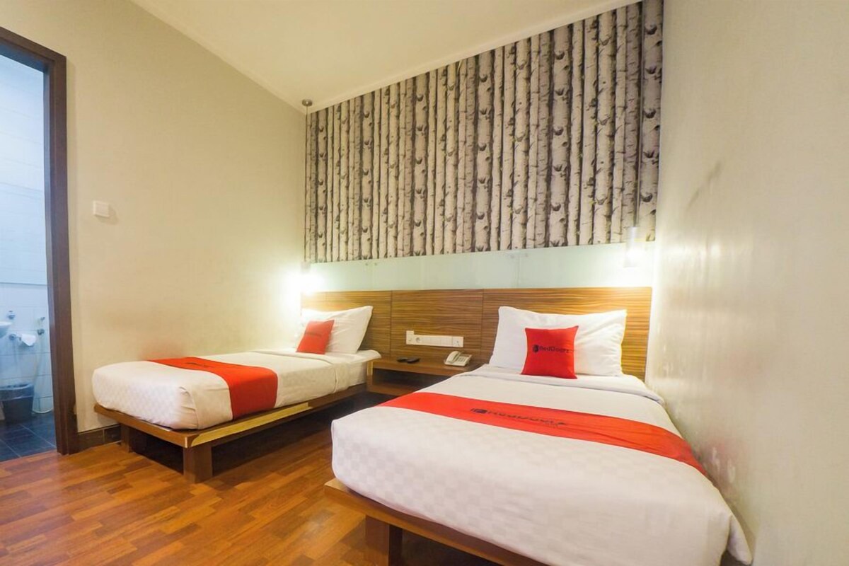 A hotel room with two beds, a wooden headboard, a patterned wall, and a wooden floor.