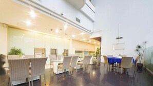 A spacious indoor area with a dining table set for six, surrounded by wicker chairs, and a glass partition separating the dining area from the rest of the space. - Reddoorz Plus @ Celaket (Malang)