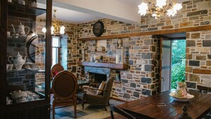 A cozy room with a stone wall, a fireplace, and a dining table with chairs. - Eudora - Mansion (Zagora-Mouresi)