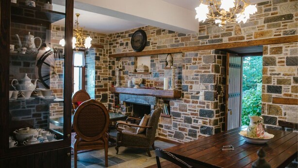 A cozy room with a stone wall, a fireplace, and a dining table with chairs. - Eudora - Mansion (Zagora-Mouresi)